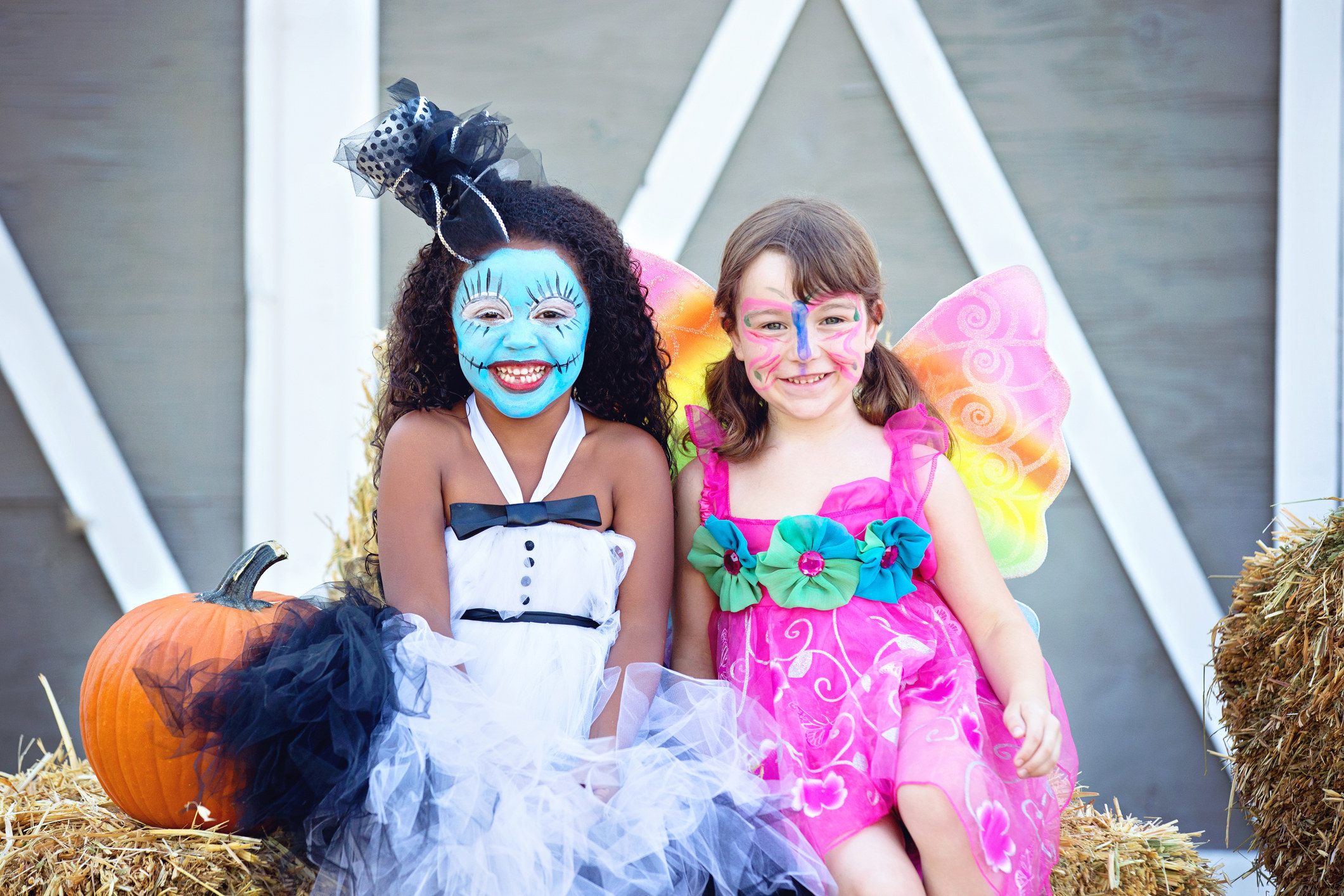 Two girls in costumes sit side by side with detailed face paint.
