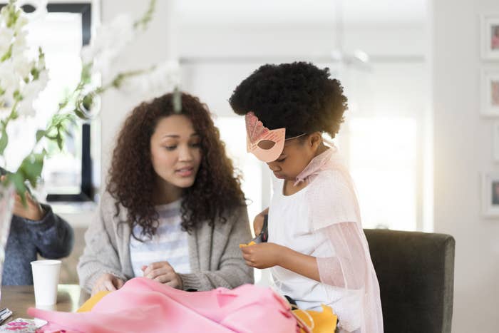 A mother and semi-costumed daughter craft with pink fabric.