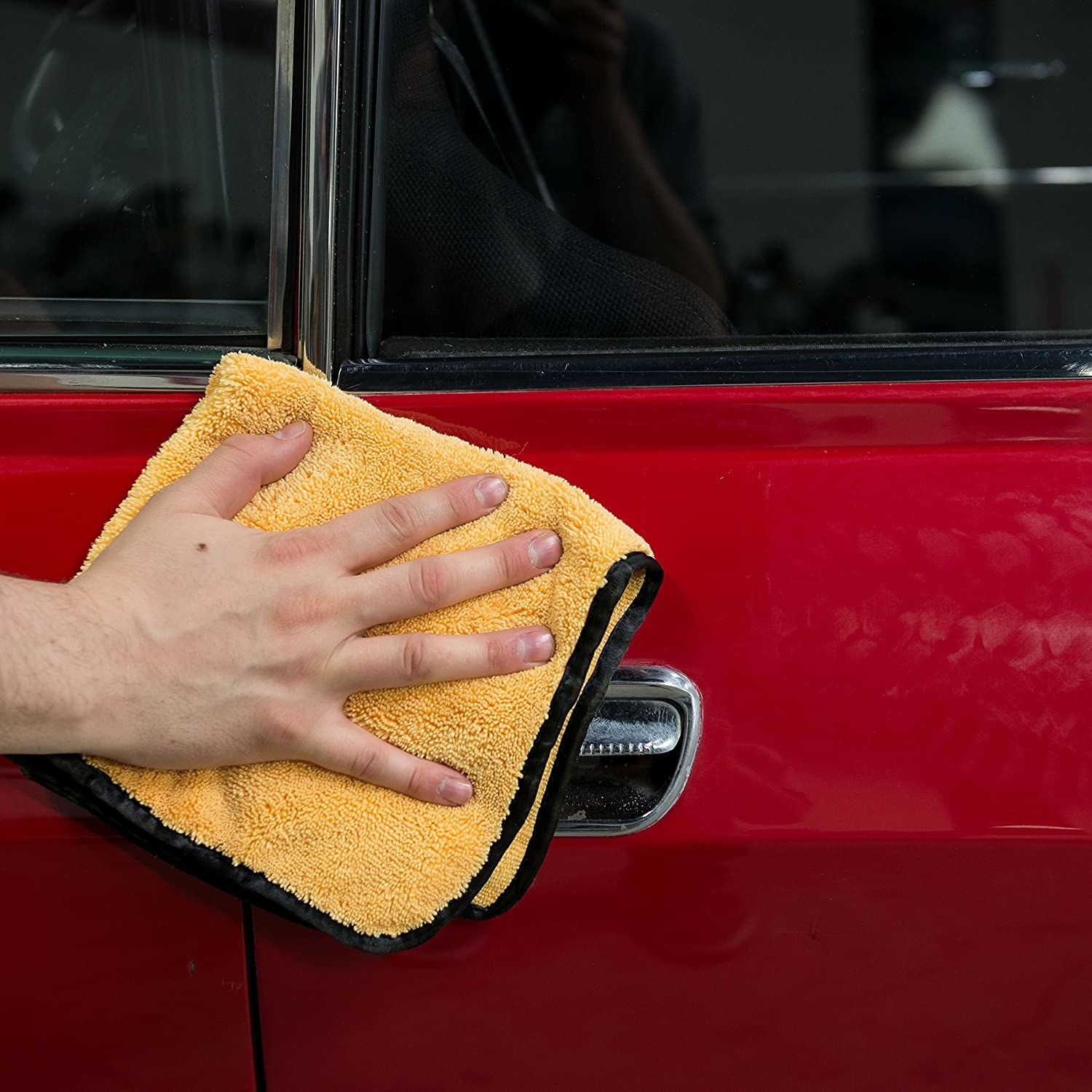 hand wiping a red car with a yellow microfiber towel with black silk trim