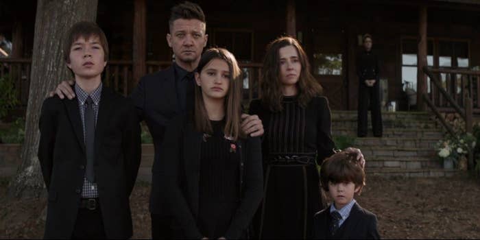 Hawkeye stands with his eldest son, middle daughter, and young son along with his wife at a funeral