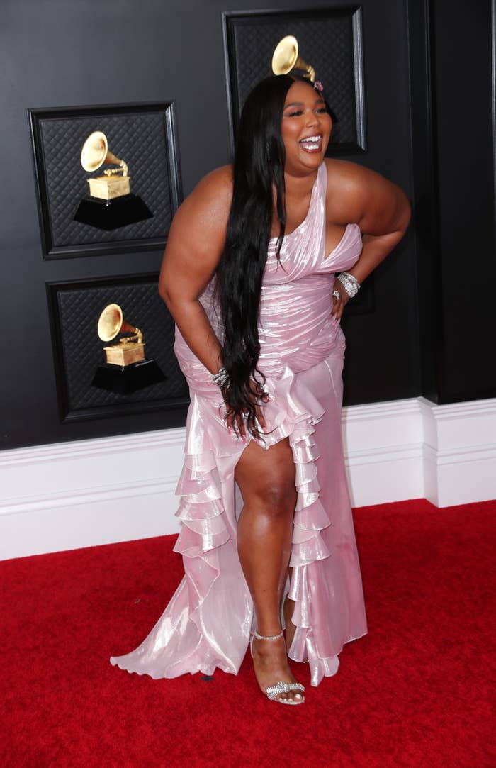 Lizzo laughing as she poses in a one-shoulder ruffled gown on the Grammys red carpet