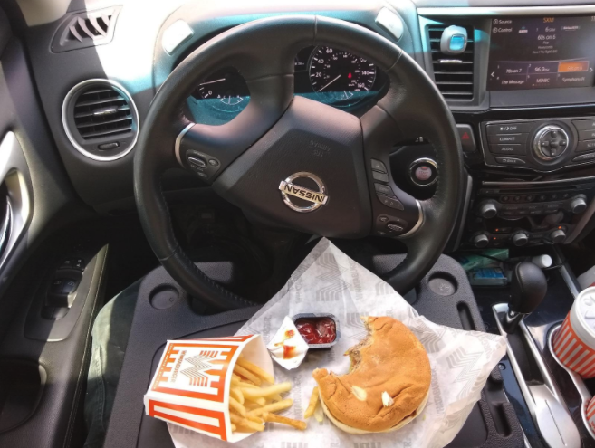 reviewer image of tray attached to steering wheel, holding up a burger and fries