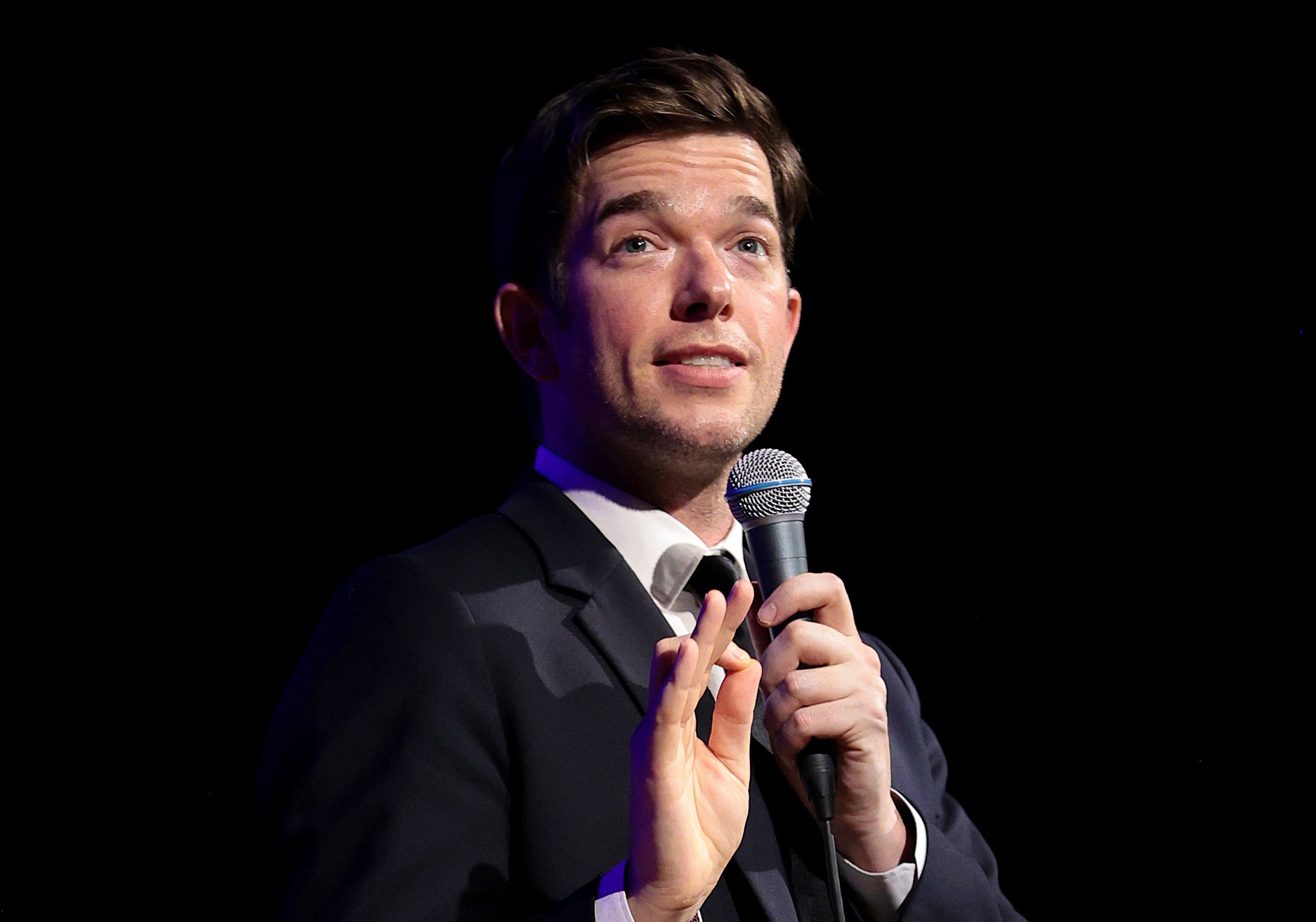 John Mulaney performing stand-up in a gray suit