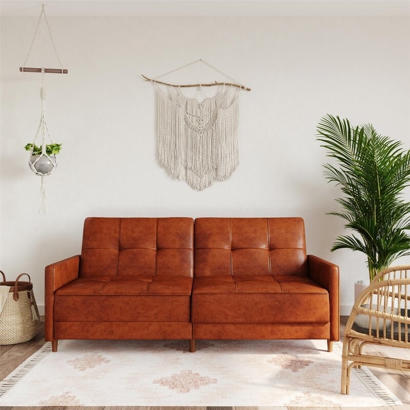 the tan faux leather couch against a white wall with boho decor