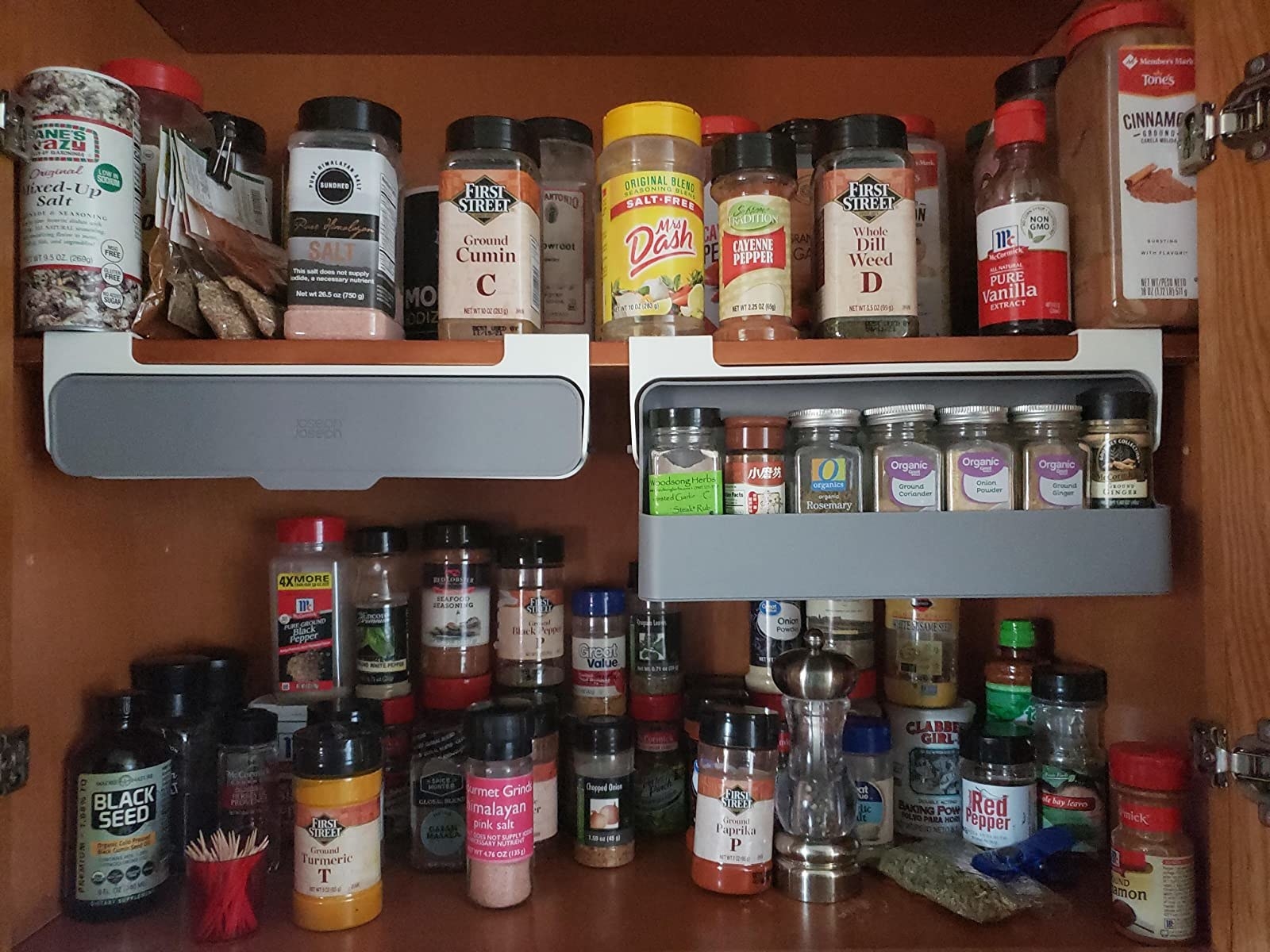 reviewer image of two of the spice racks in a cabinet — one that&#x27;s folded down showing seven spices in it and the other folded up, showing how compact it can get