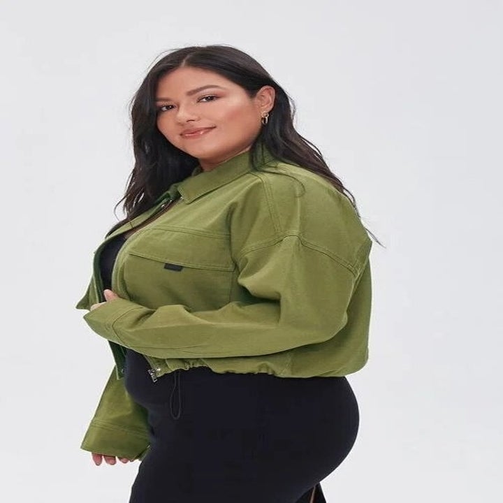 a model wearing a green drop-sleeve jacket, black dress, and sneakers