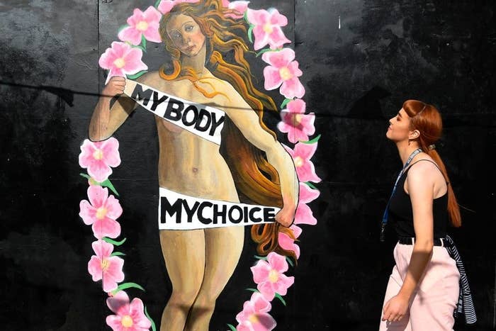 Woman walking up to a painting of "The Birth of Venus" with her holding banners and the words "My body, my choice" on them