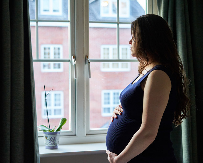 Pregnant woman looking out the window, alone