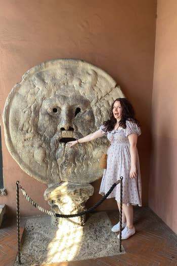 writer wearing the same dress with hand stuck in mouth of a statue