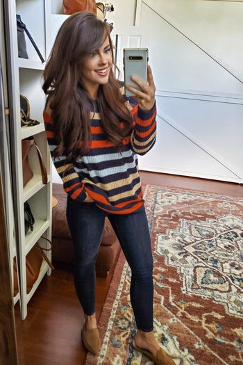 reviewer wearing a orange, blue, and brown striped sweater with dark jeans