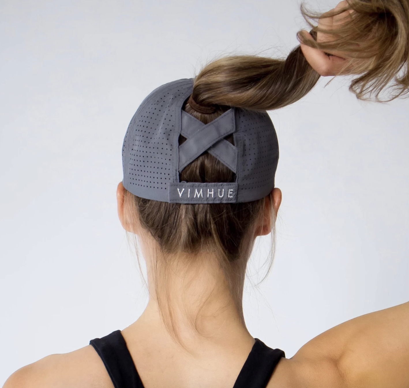 A model wearing and showing the back of the hat and how there is a slot for their ponytail