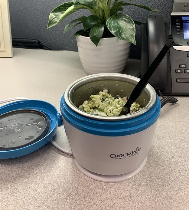 A reviewer photo of a white and blue mini crockpot with breakfast inside it sitting on a cubicle desk