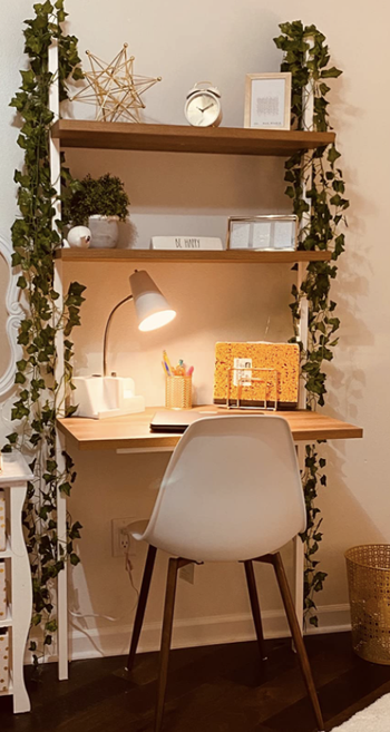 reviewer pic of three tier storage desk mounted to the wall with faux vines on either side 