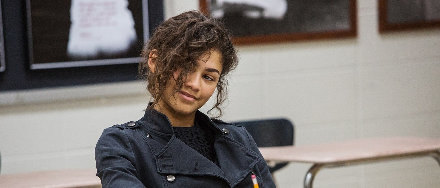MJ wearing a black jacket, hair in her face, in detention
