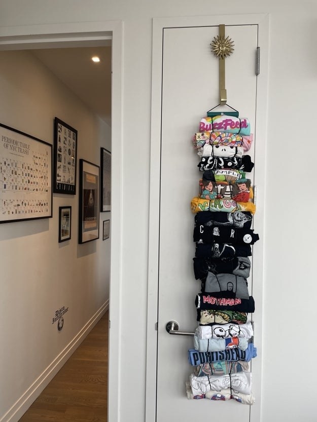 A closet door closed with several shirts hanging from a hook at the top of the door. The shirts are attached by rolling them up and putting them through stretchy loops.