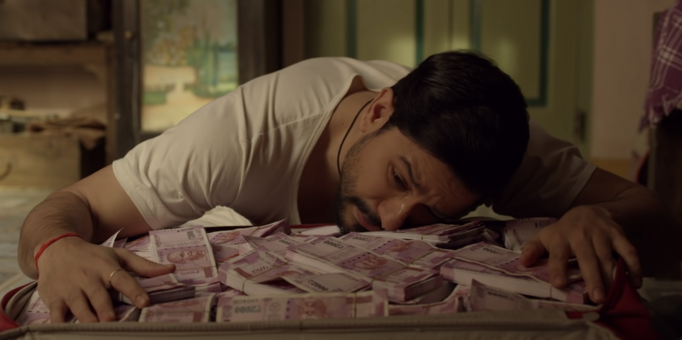 Kunal Khemu resting his head and hands on an open suitcase filled with cash
