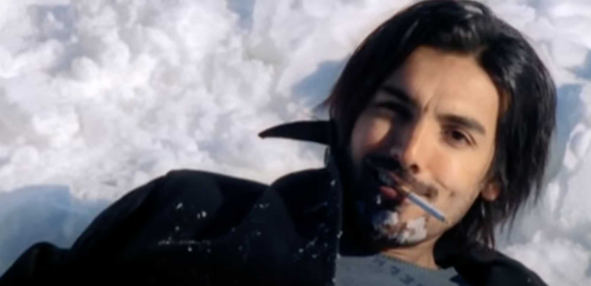John Abraham lying on a pile of snow with a cigarette in his mouth