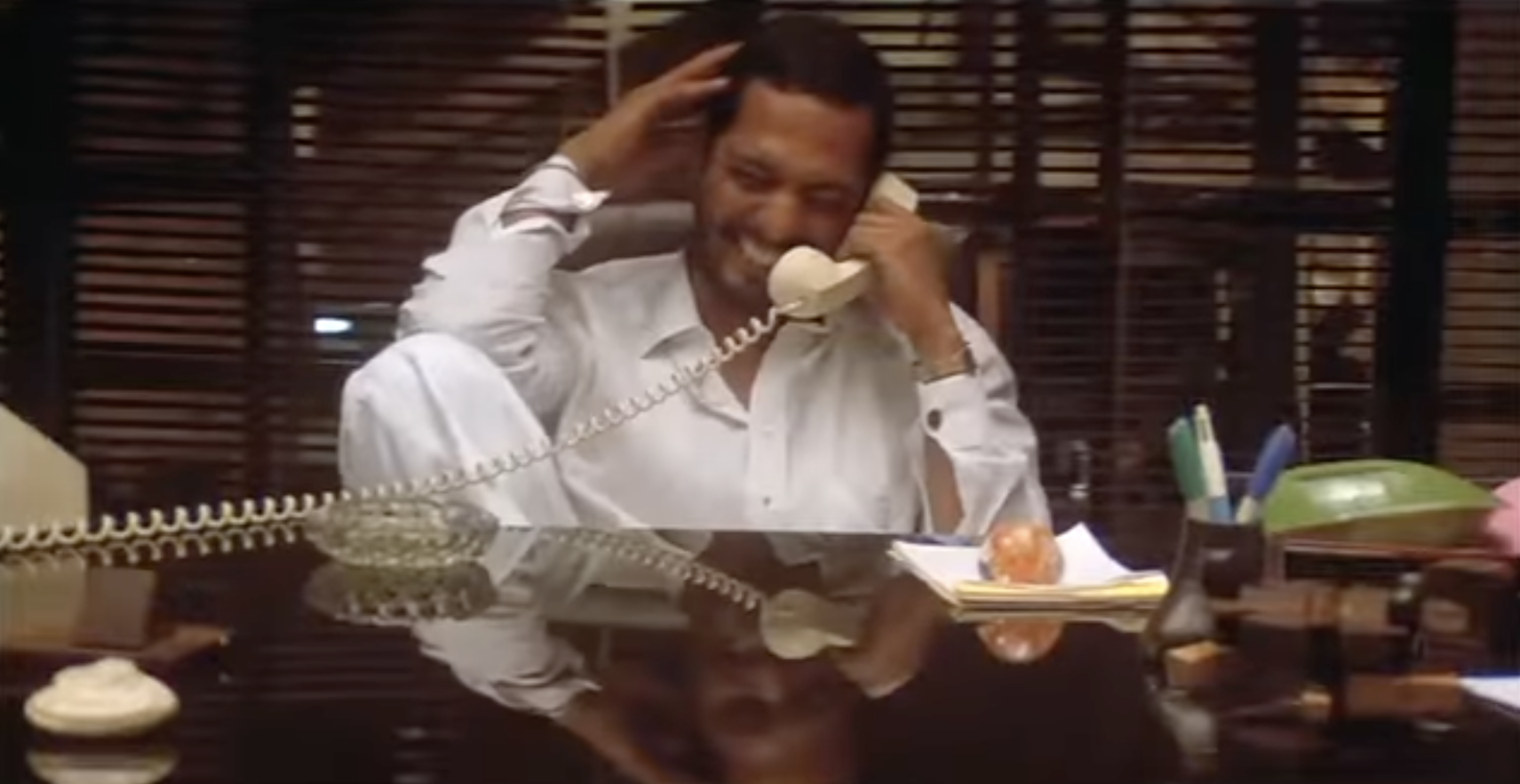 Nana Patekar laughing while holding a landline phone receiver to his ear