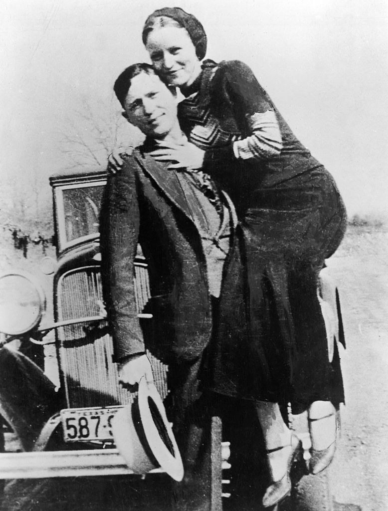 Clyde Barrow posing for a photo with Bonnie Parker in front of their car