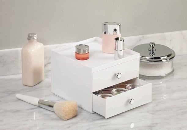 the white counter drawers with a makeup brush next to it and other bottles on it