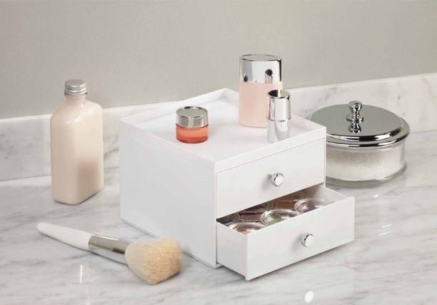 the white counter drawers with a makeup brush next to it and other bottles on it