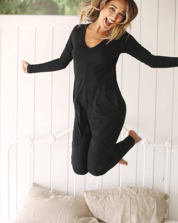A person in mid air above their bed wearing a long-sleeved romper