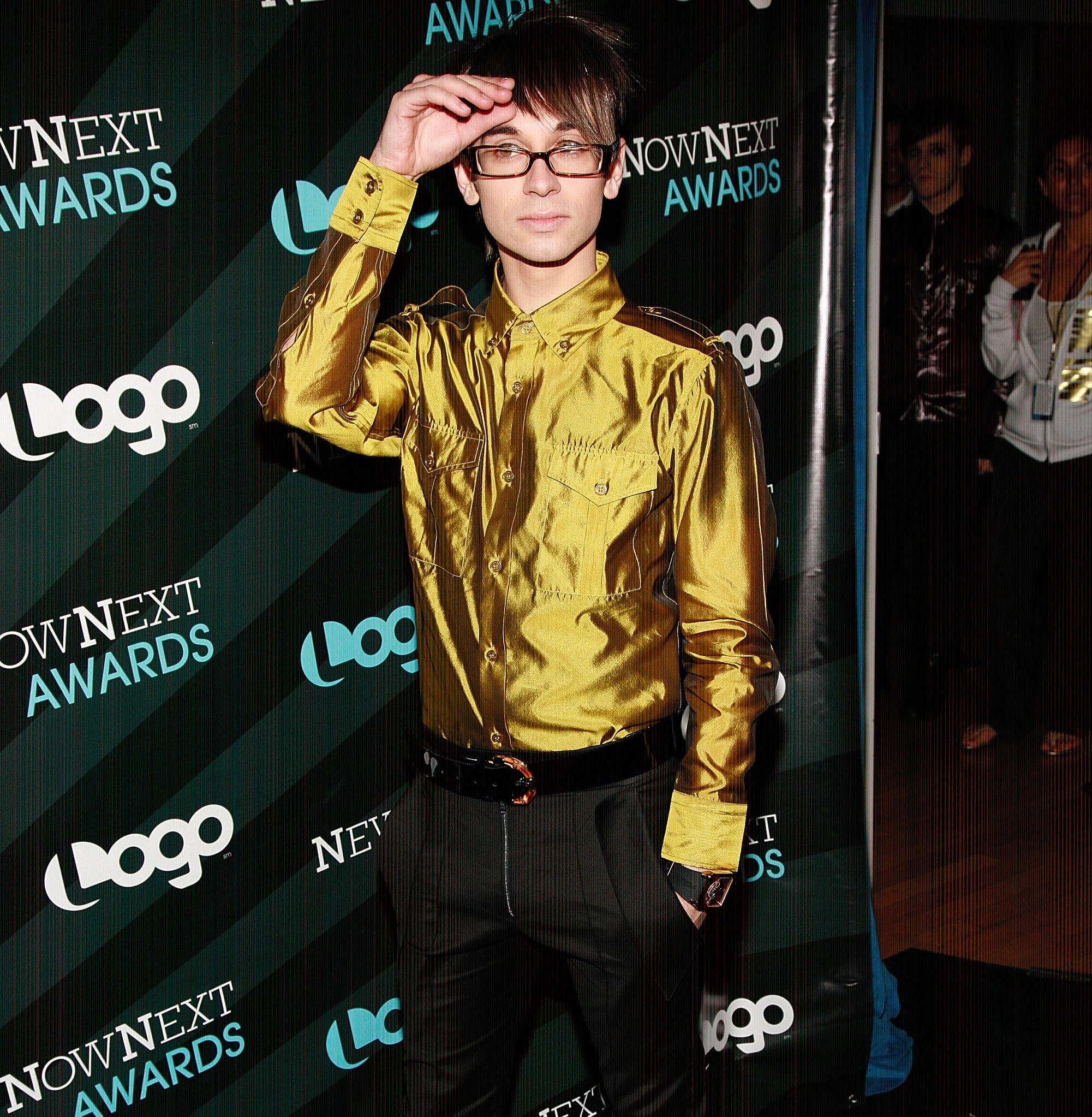 Christian Siriano wears a metallic long-sleeved shirt and dark pants on the red carpet at the Now Next Awards