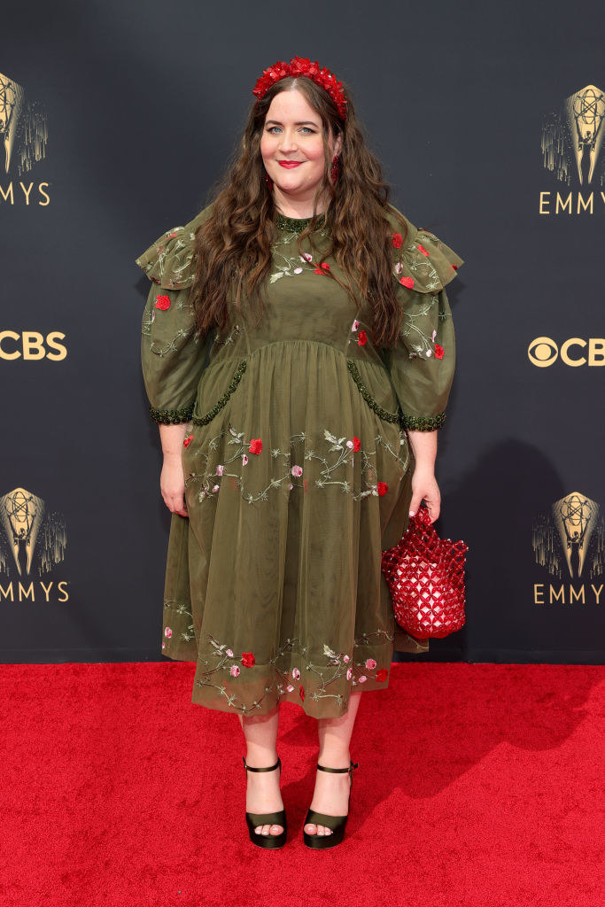 Aidy Bryant on the red carpet in a dark green calf-length dress with florals