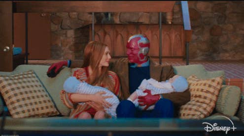 Wanda and Vision sitting on their living room couch and holding their twin boys