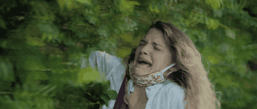 GIF of a woman wearing a mask on her chin getting hit in the face with a tree branch