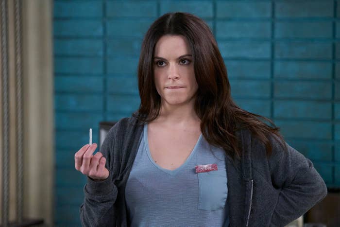 Emily Hampshire holds a thin white item between her fingsers