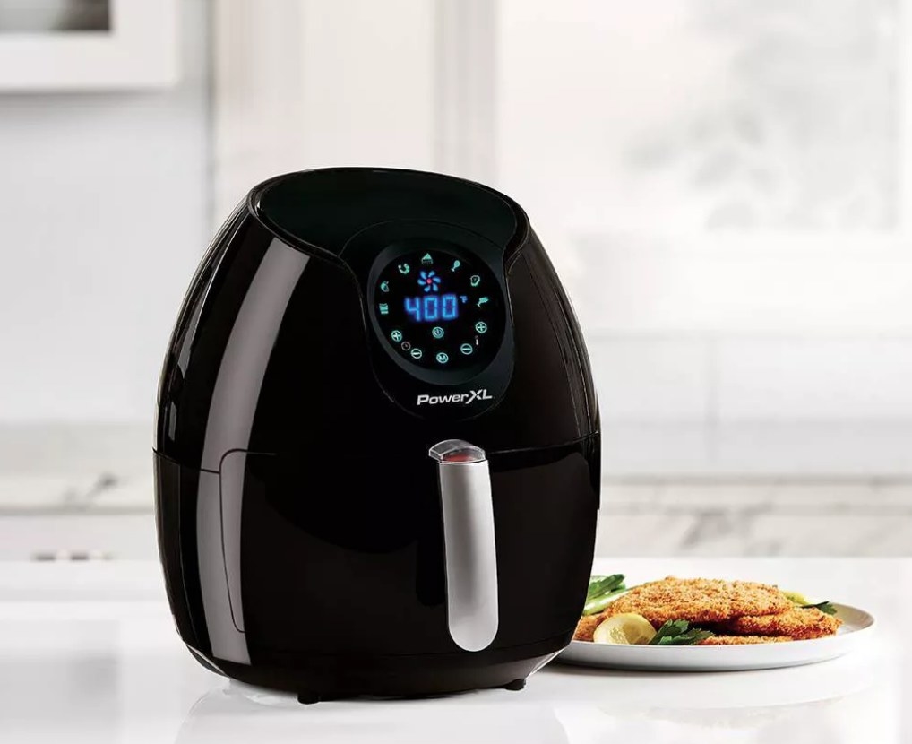 A black air fryer on the kitchen counter next to air fries chicken