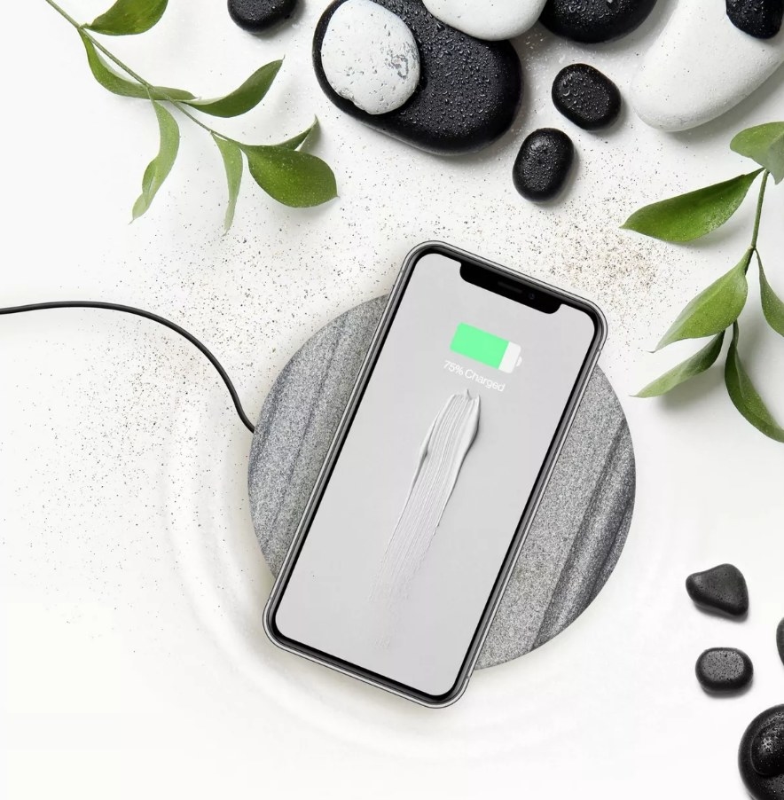 A round, grey/black sand stone charging pan with an iPhone atop
