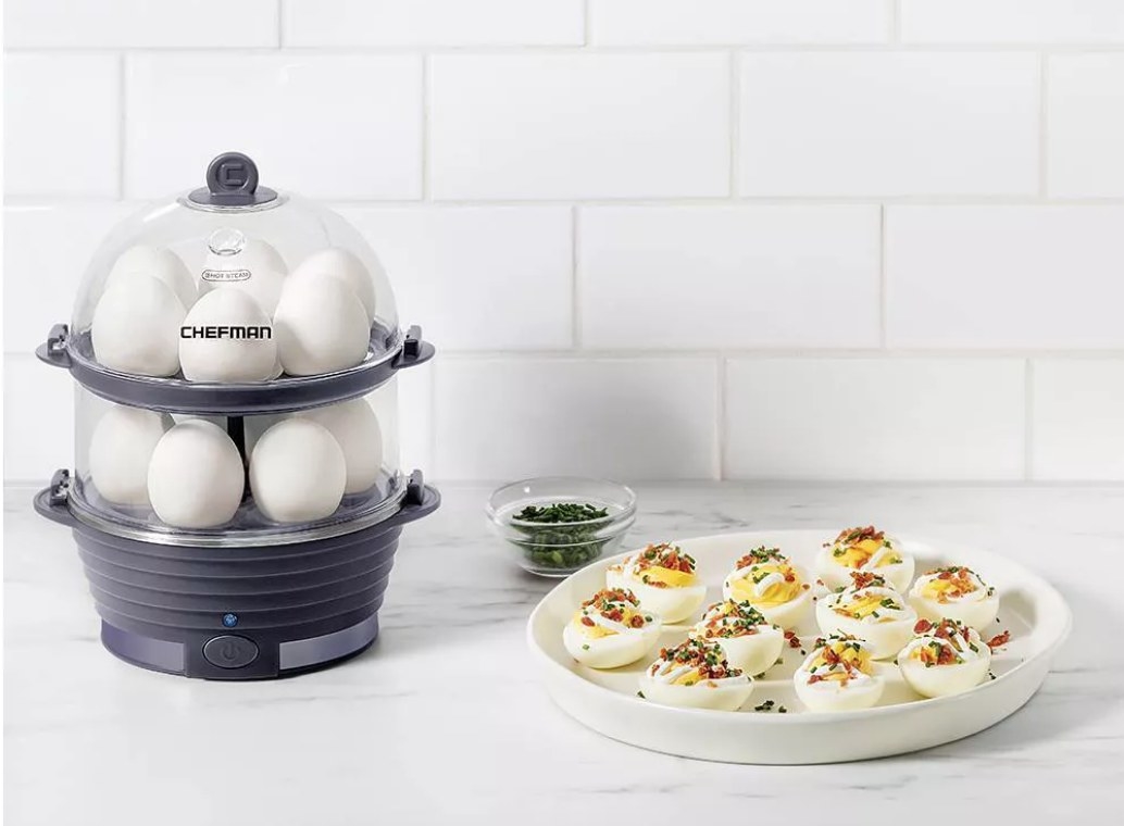A navy, 12-egg, egg cooker filled with hard boiled eggs on a kitchen counter next to a plate of deviled eggs