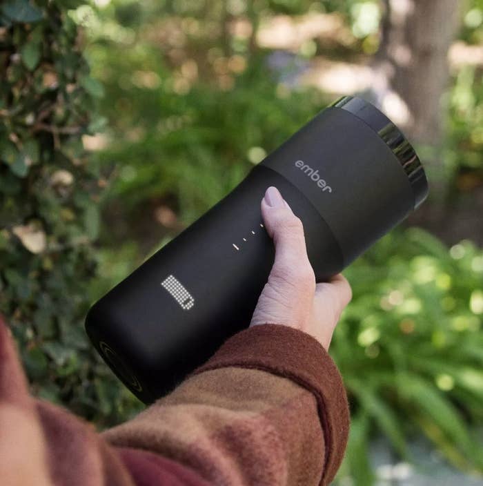 A model holding a black, temperature controlled travel mug