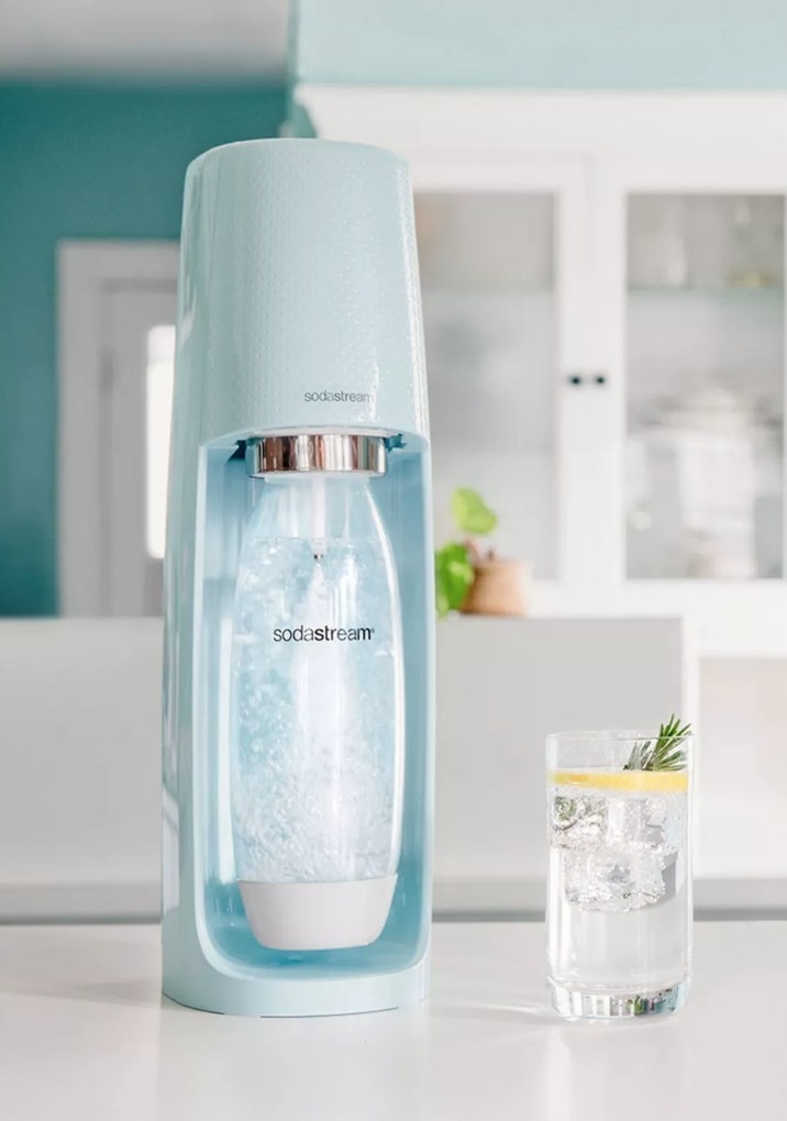 A blue Sodastream next to a glass of sparkling lemon water
