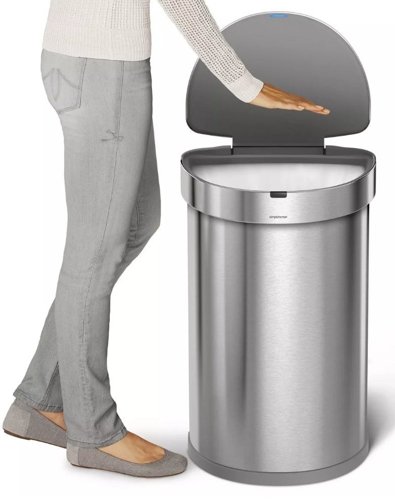A model waving their hand over a silver, motion-sensor trash can