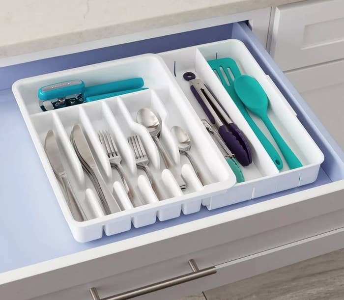 A white, expandable utensil organizer filled with spoons, knives, and forks