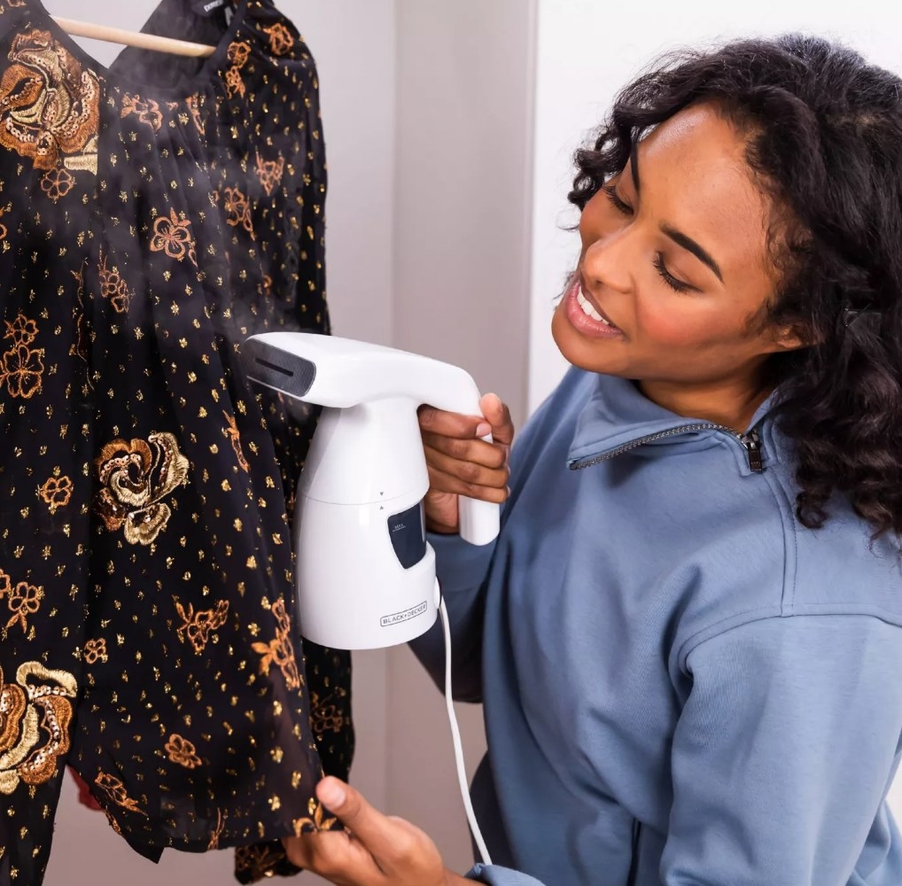 A model using a white, handheld steamer on a blouse
