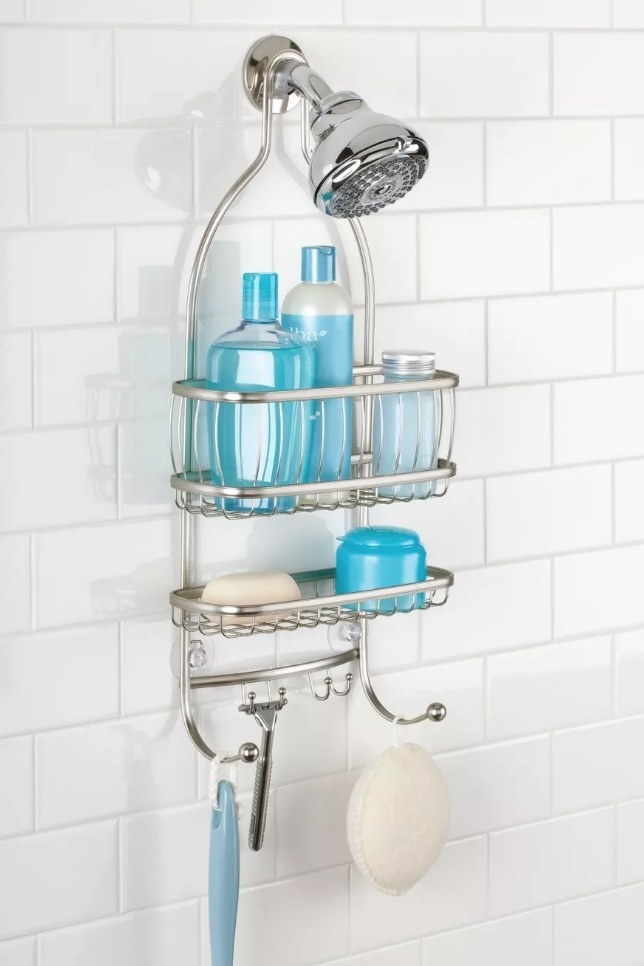 A silver, metal shower caddy hanging over the shower head filled with soaps with a loofa hanging off the bottom hook