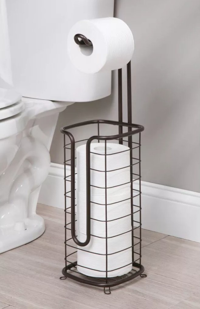 A bronze, metal freestanding toilet paper holder filled with three rolls and one on the hook atop