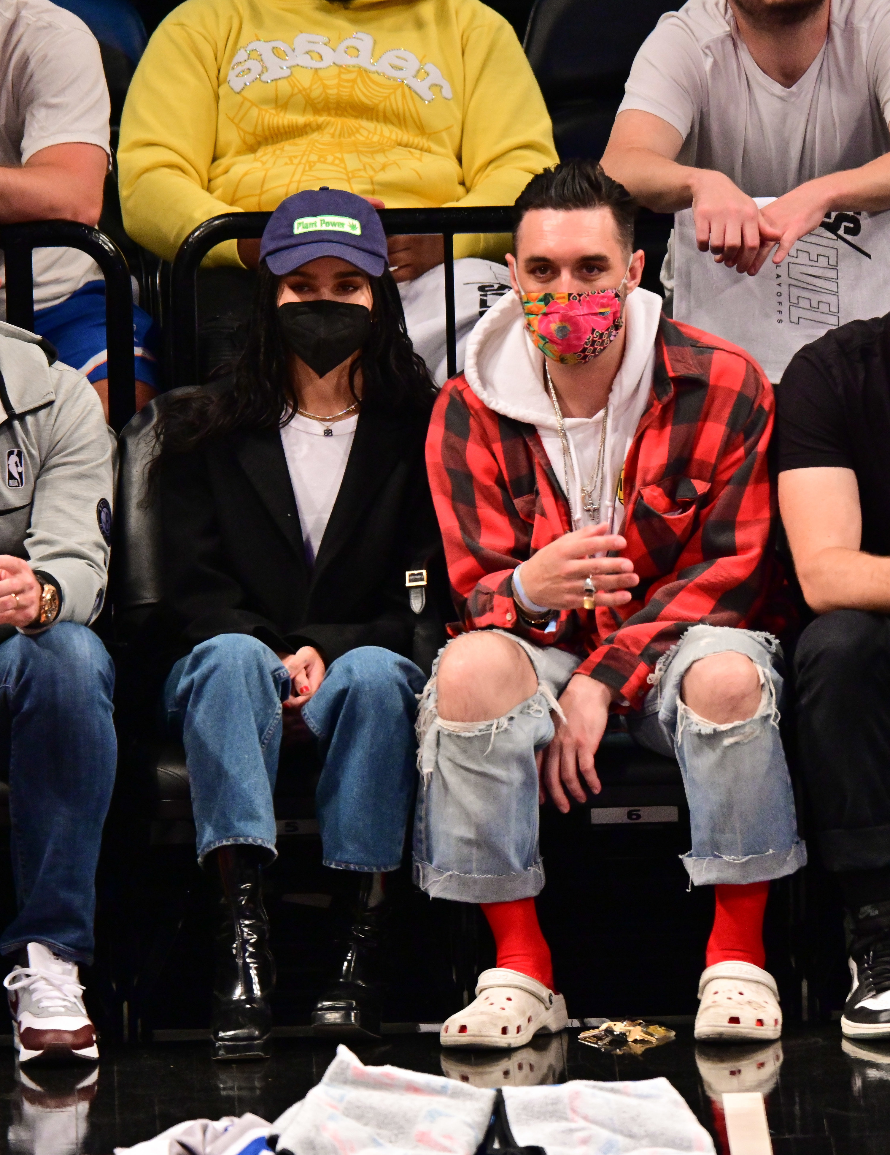 Zoe sitting courtside in jeans boots t-shirt cardi hat and mask