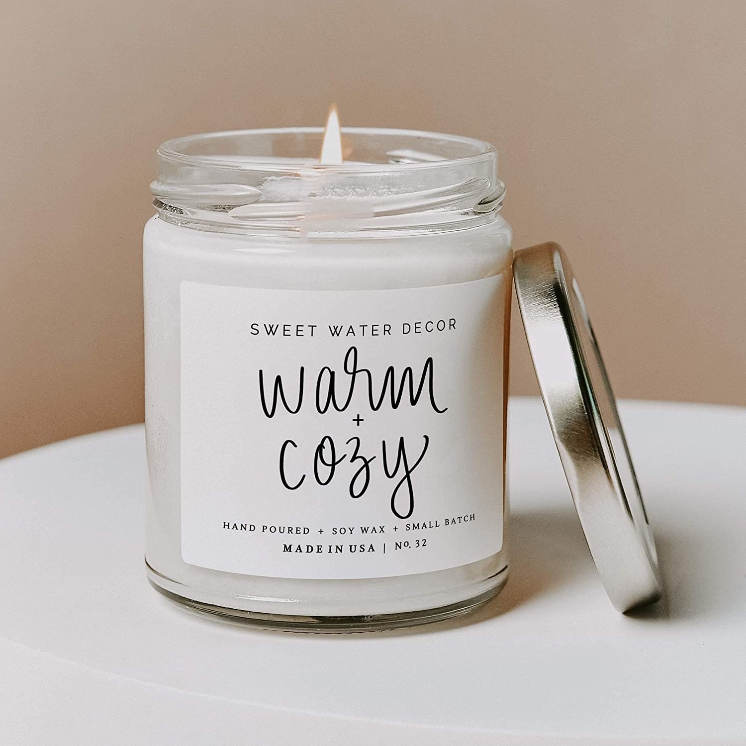 a candle with a white label on it that says &quot;warm + cozy&quot;