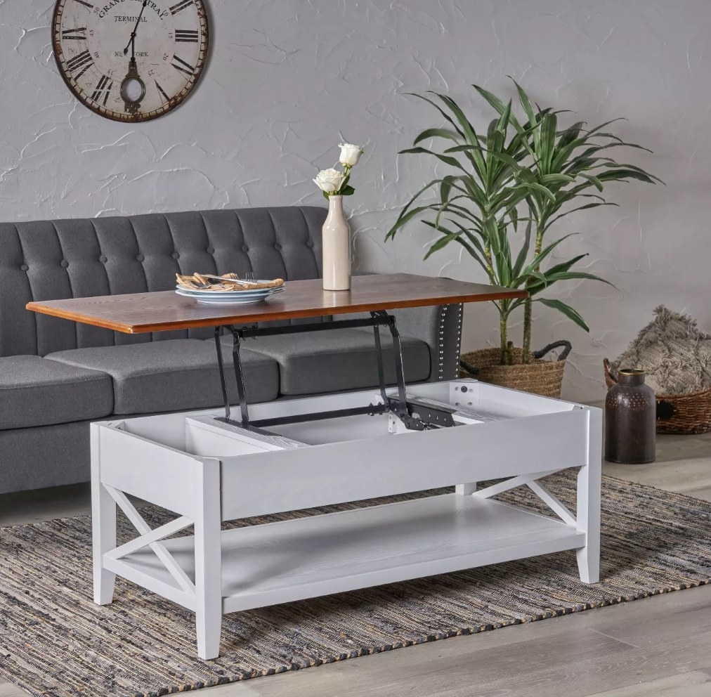 A white coffee table with a brown lift top and one shelf at the base in a living room