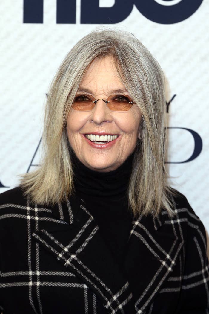 Diane Keaton, wearing a checkered coat and dark turtleneck, smiling at a red carpet event