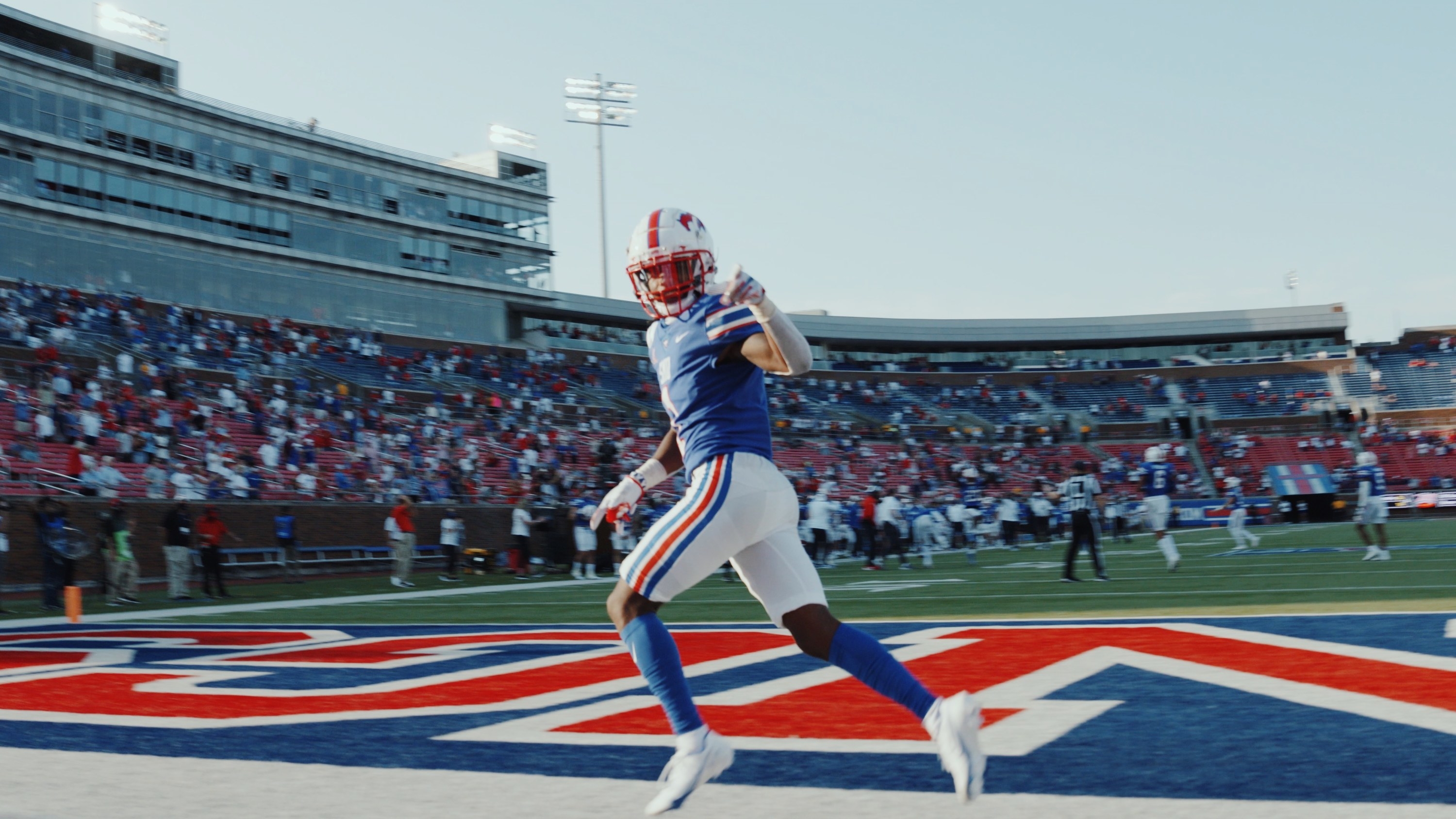 A football player looks and points to the camera from the touchdown zone of a football field