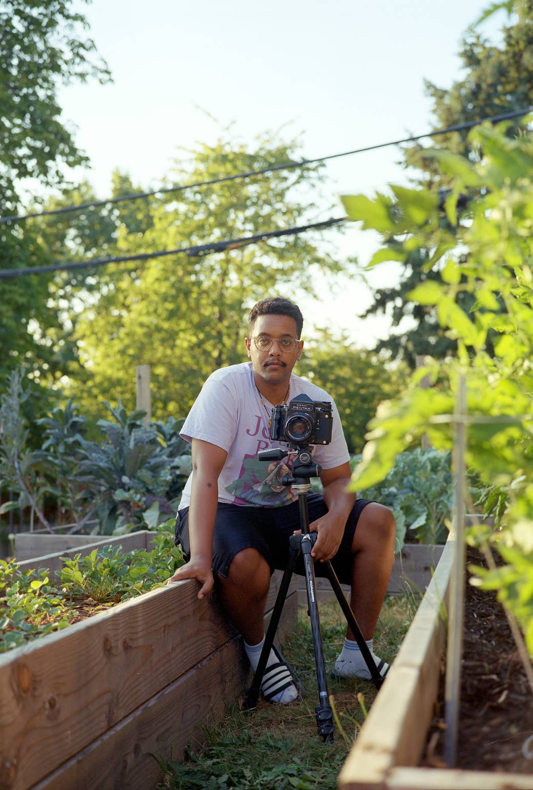 The photographer sits in his garden with a medium format camera, facing the camera