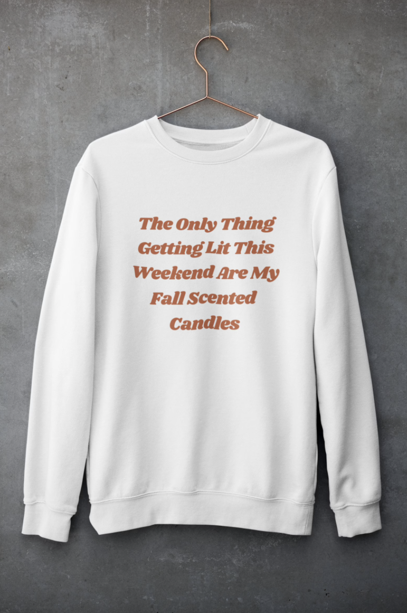 white sweatshirt with the words "the only thing getting lit this weekend are my fall scented candles" on it in orange