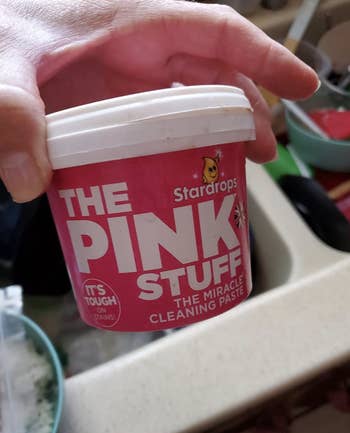 reviewer photo of them holding a pink jar of cleaning paste
