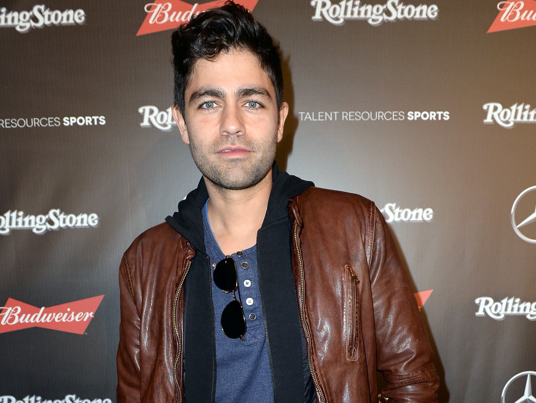 Adrian wears a brown leather jacket and black hoodie